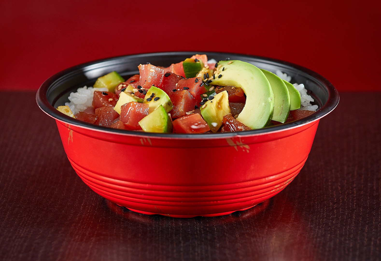 Spicy Tuna Poke Bowl: Fresh ahi tuna and avocado with black sesame seeds served in a traditional red bowl.