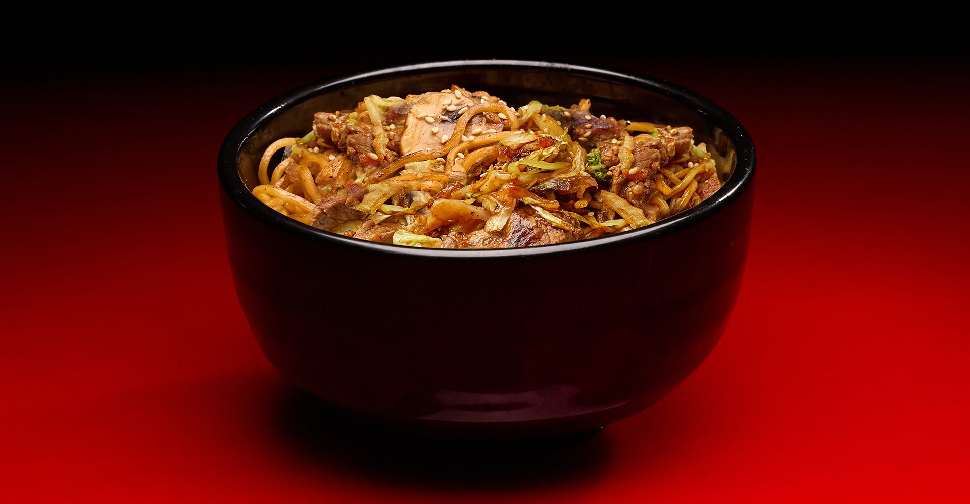 Yakisoba Steak Bowl in traditional black bowl against gradient red background
