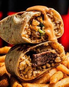A burrito cut in half and sitting on top of fries with sauce running down it.